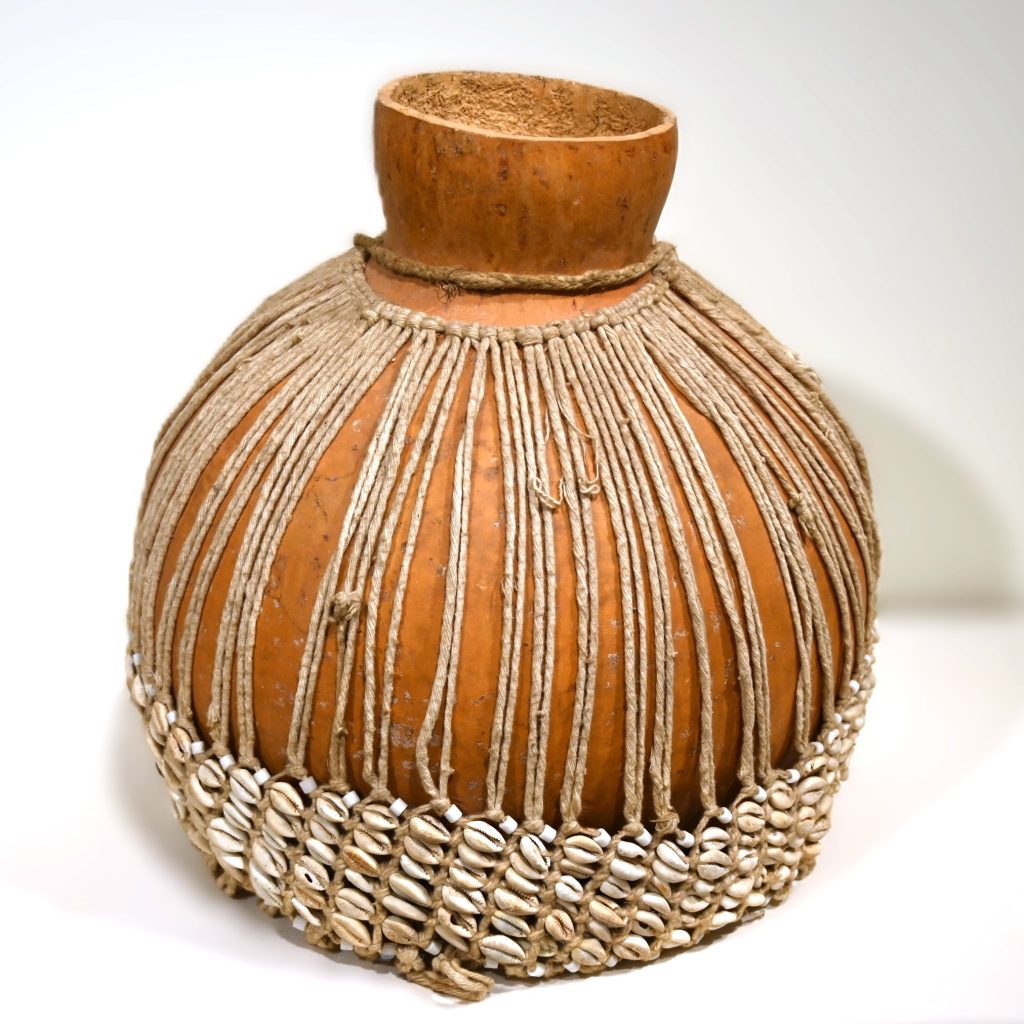 large gourd with strings around it and cowrie shells around the bottom portion